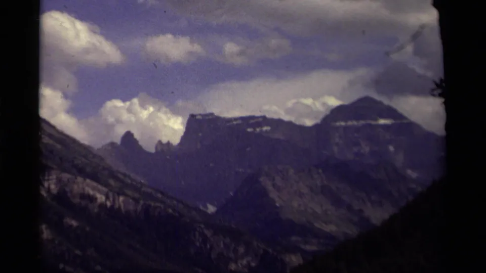 1979 8mm view of Canadian high peaks, dark valley slopes, and cloudy sky with grain and color fading.