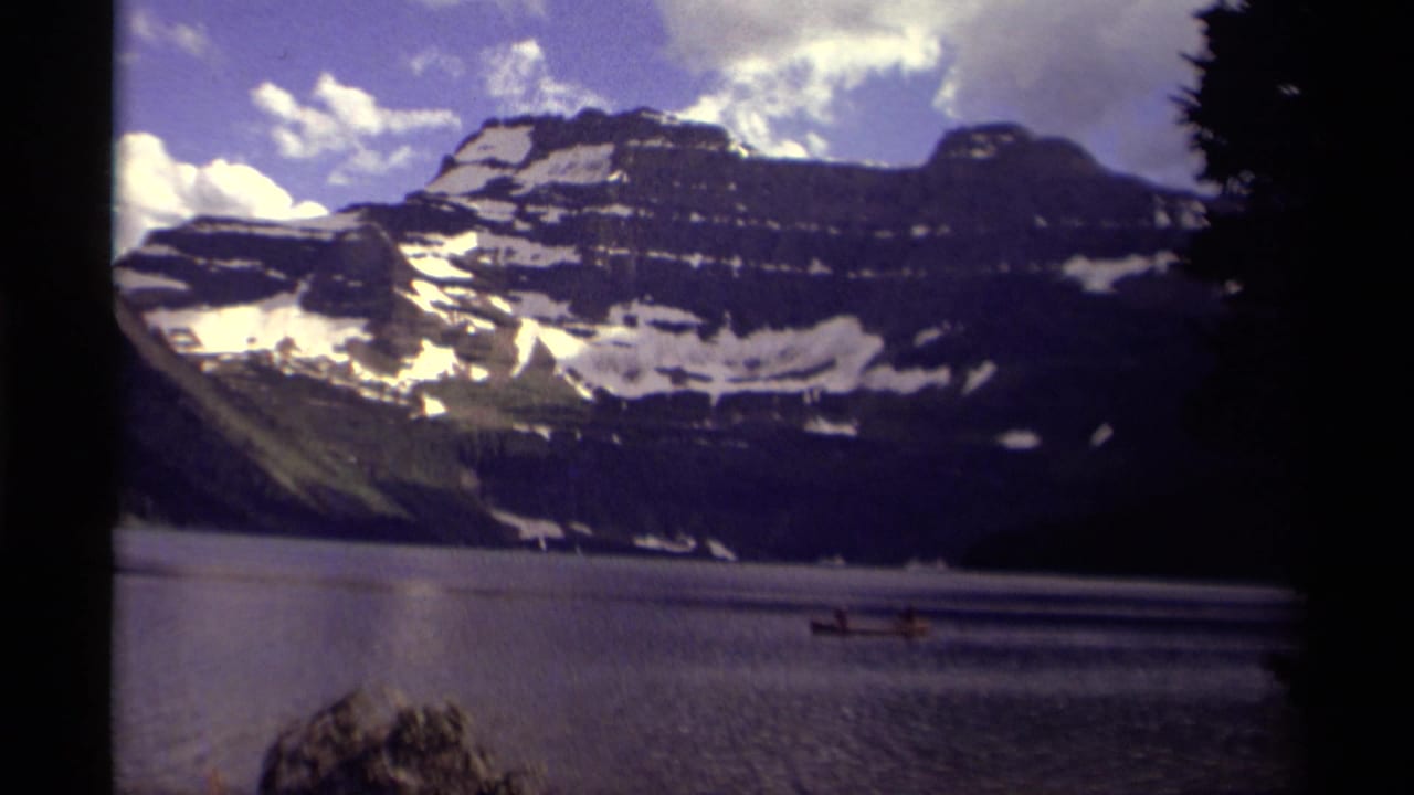 Small boat on a mountain lake below snow-striped peaks and a partly cloudy sky.