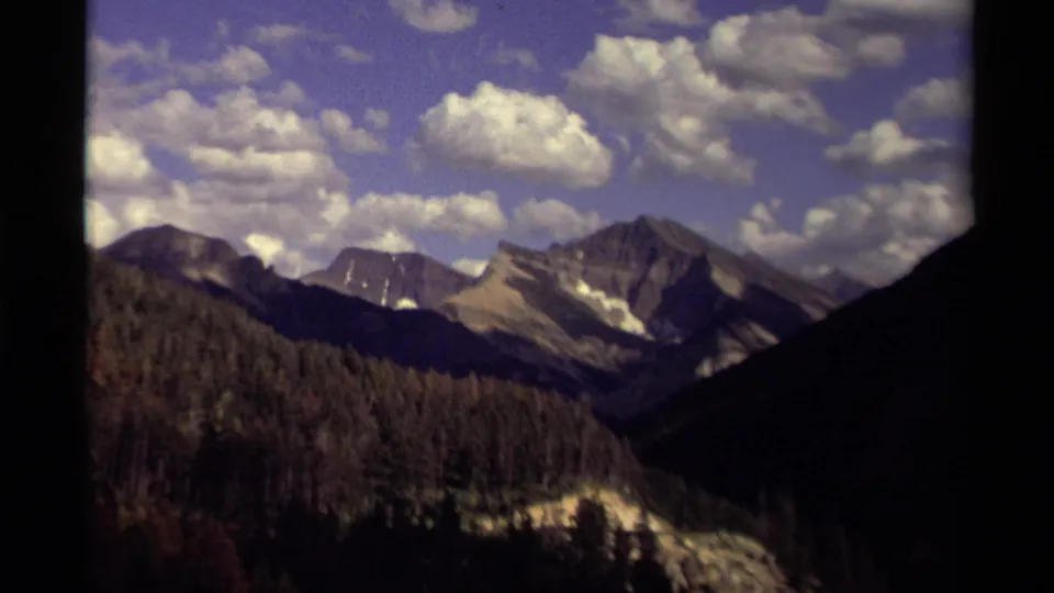 1979 Canada 8mm frame showing rugged alpine peaks rising behind dense forest, with soft grain and motion blur.