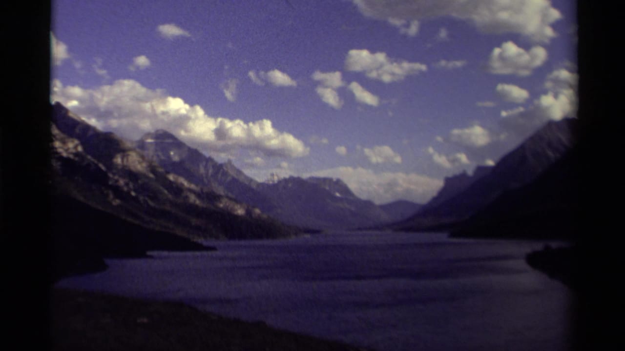 Canadian mountain lake landscape on 1979 8mm film, with cloud cover, distant ridges, shadowed shoreline, and visible gate edges.