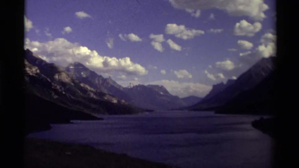 Canadian mountain lake landscape on 1979 8mm film, with cloud cover, distant ridges, shadowed shoreline, and visible gate edges.