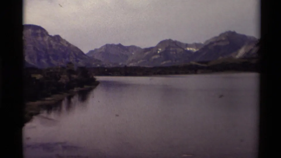1979 Canadian home-movie view of a shaded shoreline, still lake water, distant mountain slopes, and visible 8mm frame borders.