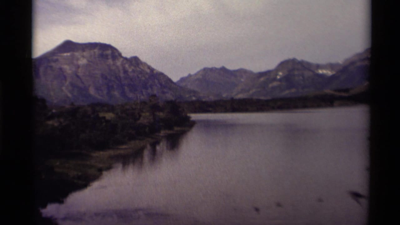 Mountain lake with rugged peaks, tree-lined shore, overcast sky, and visible film frame edges.