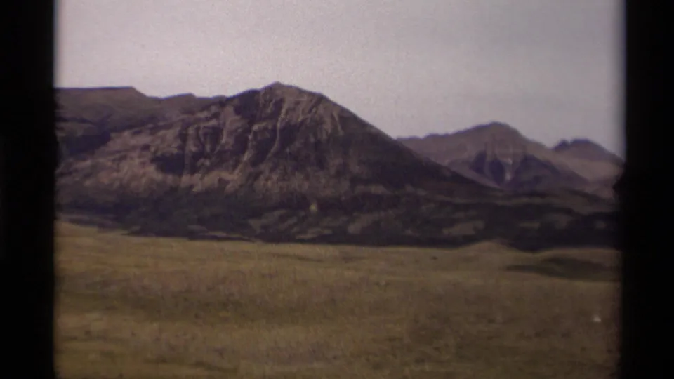 1979 Canadian landscape frame showing grassland, low rolling terrain, and layered rocky mountains in soft 8mm color.