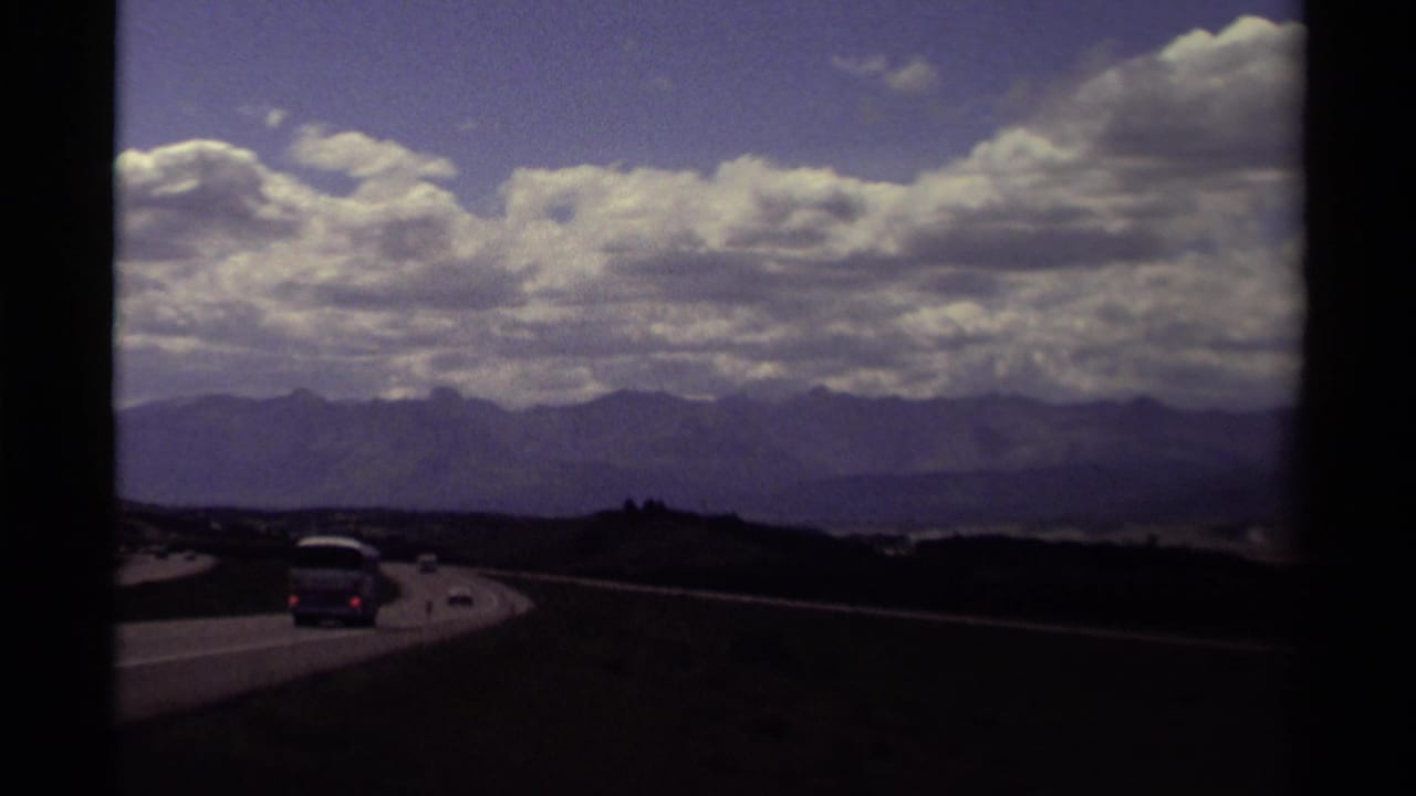 Cars travel on a divided highway with mountains and layered clouds in the distance.