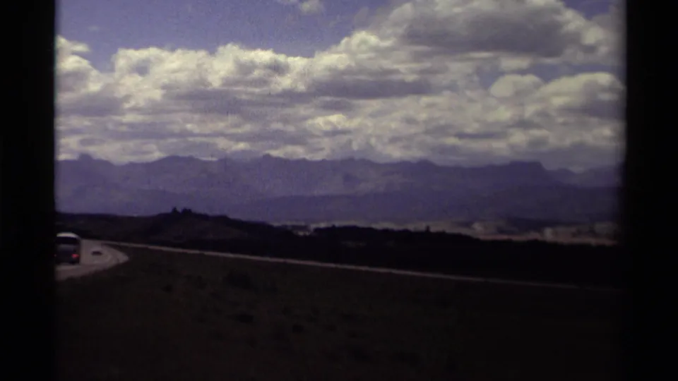 Canadian 8mm travel footage from 1979 showing a highway bend, a car near the frame edge, dark foreground hills, and distant mountains.