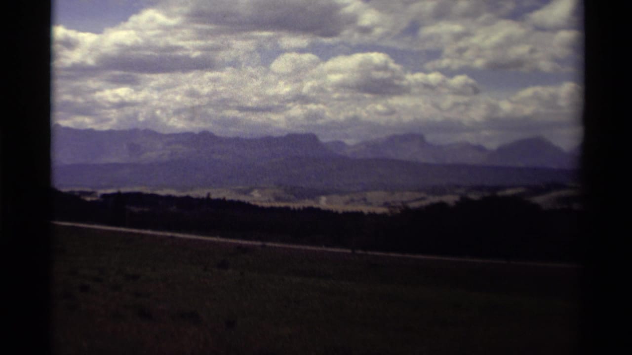 1979 Canadian 8mm frame showing distant mountain ridges under a cloud-filled sky from a moving travel viewpoint.