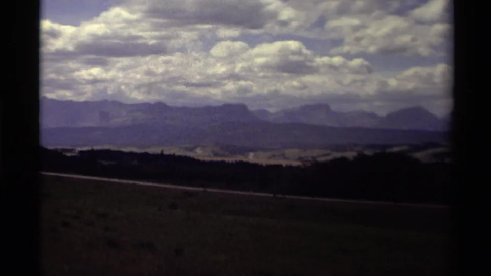 1979 Canadian 8mm frame showing distant mountain ridges under a cloud-filled sky from a moving travel viewpoint.