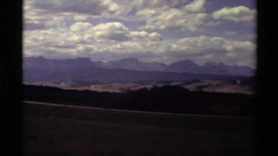 Canadian 8mm travel frame with layered clouds above distant blue-purple mountains and open terrain.
