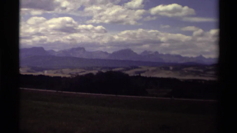 1979 Canadian home-movie frame showing mountains, bright clouds, and open roadside terrain from a moving vehicle.