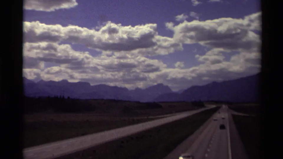 1979 8mm home-movie view of cars on a Canadian highway leading toward distant mountains beneath layered clouds.