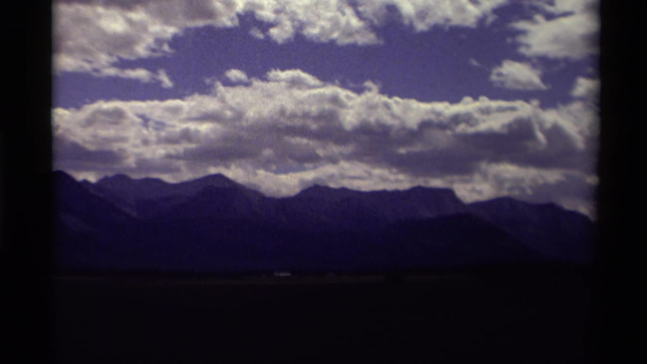 Dark mountain range beneath a blue sky filled with bright white clouds.