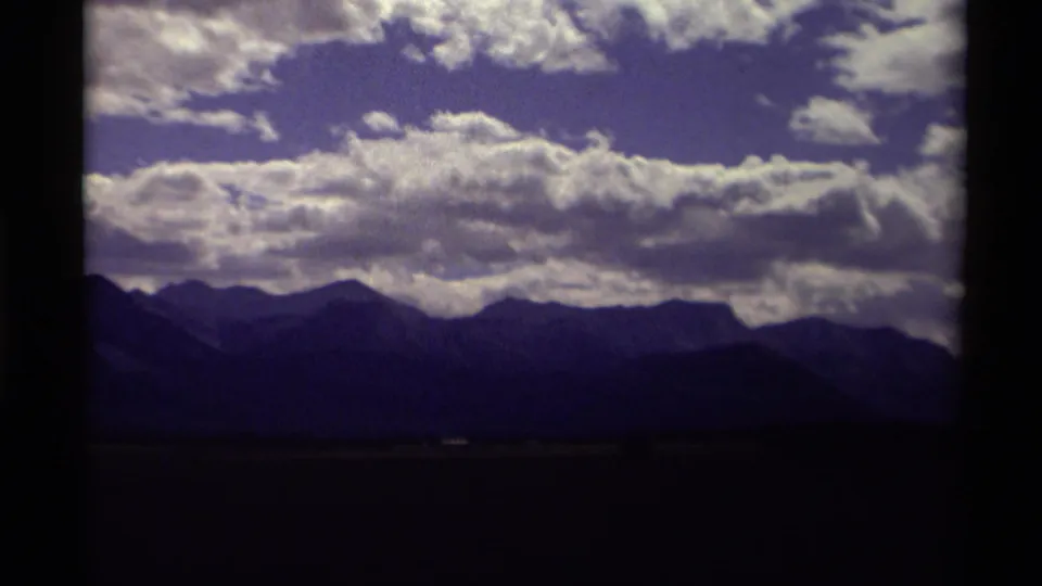 1979 Canadian 8mm frame showing distant dark mountains under a saturated blue sky with large white clouds.