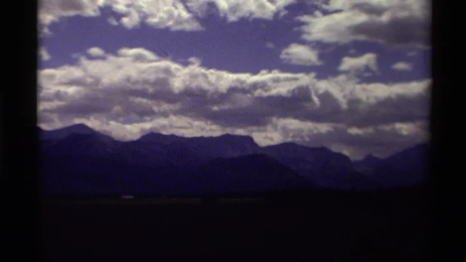 1979 Canadian 8mm view of a mountain horizon beneath broad white clouds and a dark foreground.