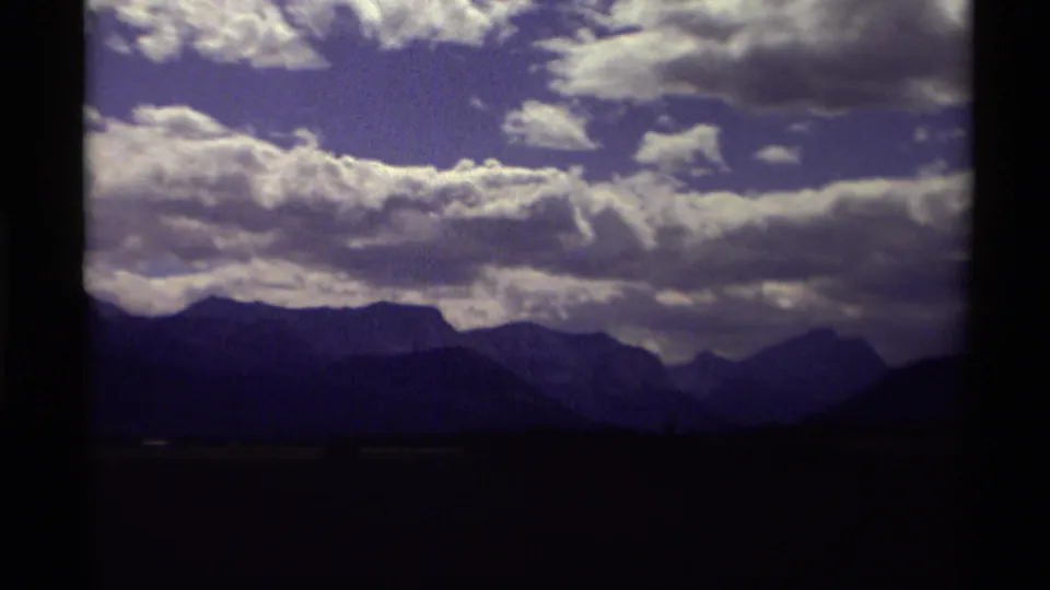1979 Canadian 8mm frame with layered mountain ranges and dense clouds crossing the blue sky.