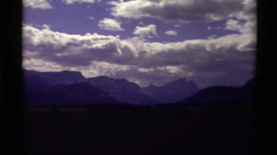 1979 Canadian 8mm scenic frame showing a distant mountain range below bright white clouds and blue sky.