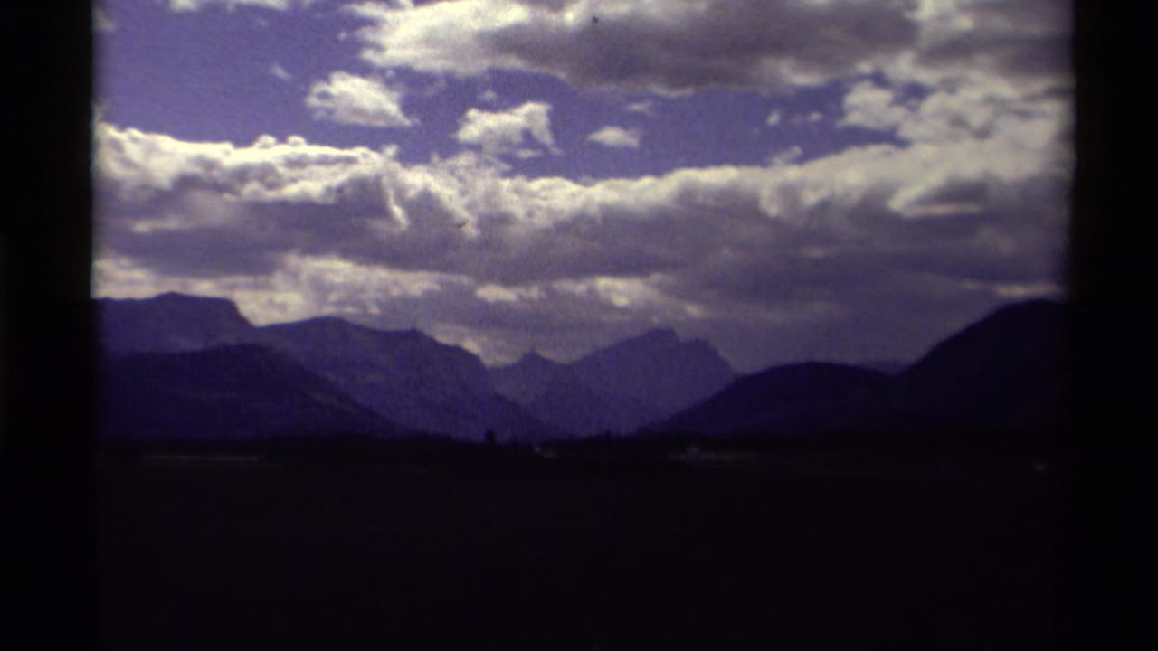 Dark-framed view of distant mountain ridges under bright clouds.
