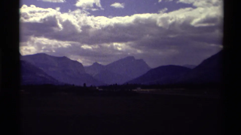 8mm home-movie view from Canada in 1979 showing mountain ridges, a shadowed valley, and bright clouds across the sky.