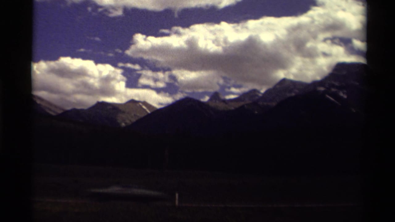 1979 Canadian 8mm travel view of shadowed mountain ridges under bright clouds, framed by dark window or film edges.