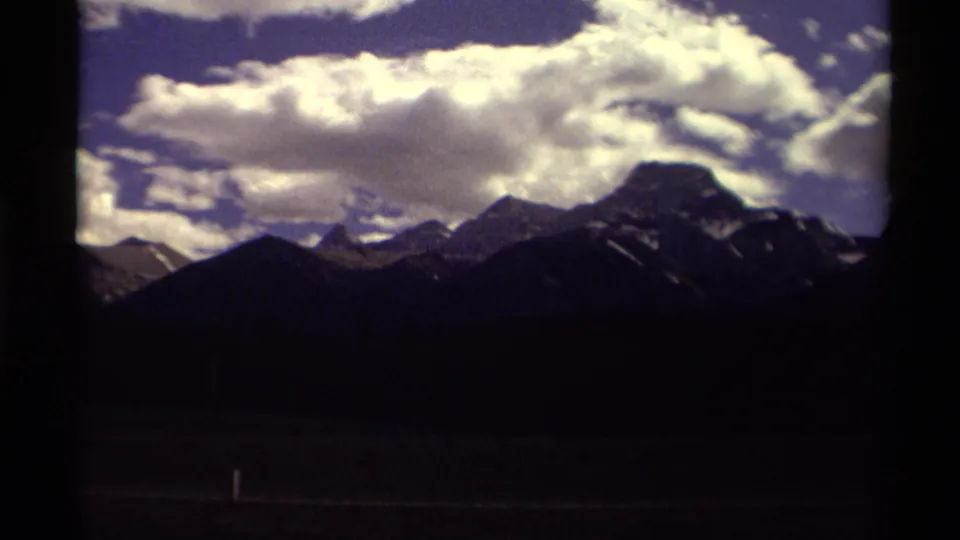 Canadian mountain skyline under billowing clouds, with dark 8mm frame or window borders emphasizing a traveler viewpoint.