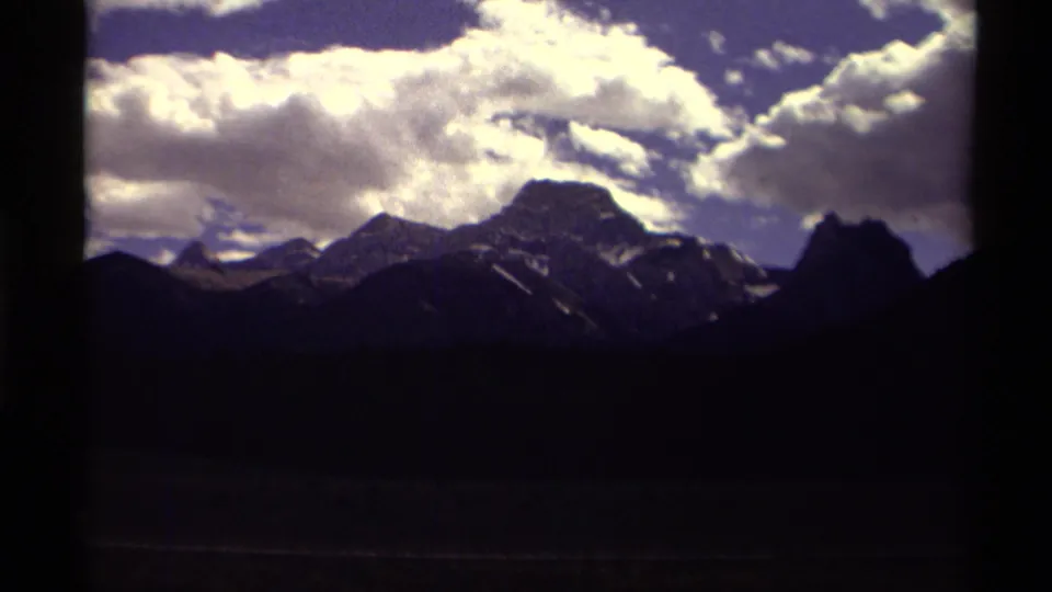 Saturated 8mm frame of Canadian mountains and heavy white clouds, with the lower landscape falling into deep shadow.