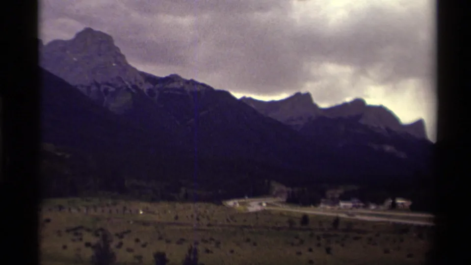 1979 Canada 8mm frame with a roadside settlement and small vehicles visible below steep, shadowed mountain slopes.