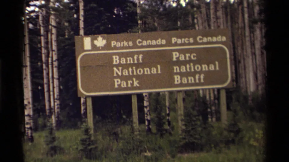 1979 8mm close view of the bilingual Banff National Park sign with Parks Canada text and birch trees behind it.