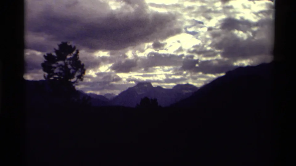 1979 8mm scenic view of Canadian Rockies mountain silhouettes under a dramatic, cloud-filled sky.