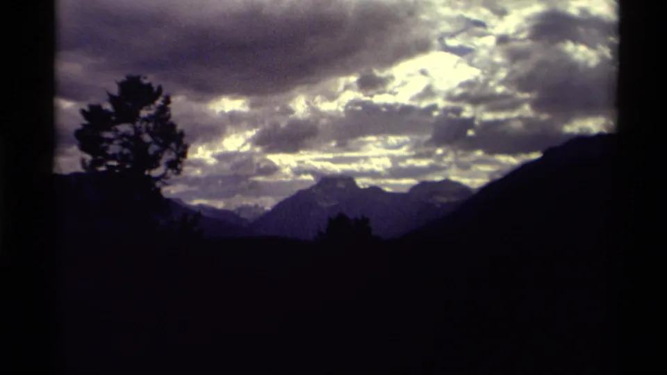 Vintage 8mm view of a Canadian mountain horizon, framed by a dark tree and glowing cloud cover.
