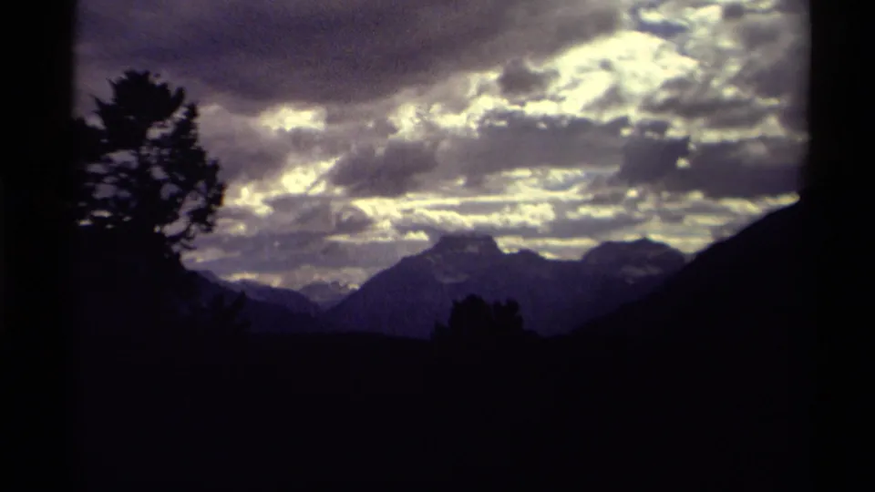 1979 Canadian mountain landscape on 8mm film, with a silhouetted tree and distant peaks below dense clouds.