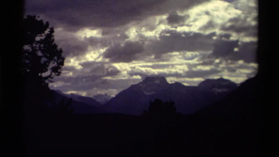 End frame of 1979 Canada 8mm footage showing a dark mountain range and trees beneath glowing cloud cover.