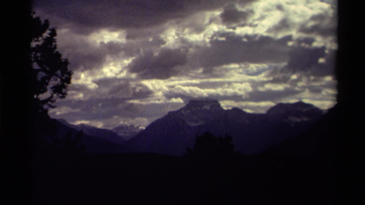 1979 8mm home-movie view in Canada of silhouetted mountains beneath a moody cloud-filled sky, framed by dark trees.