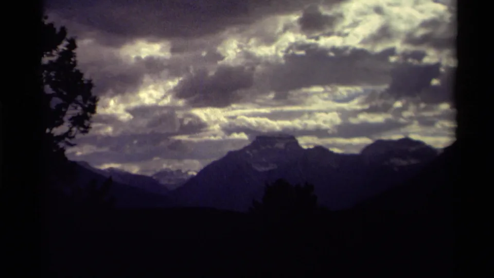 1979 8mm home-movie view in Canada of silhouetted mountains beneath a moody cloud-filled sky, framed by dark trees.