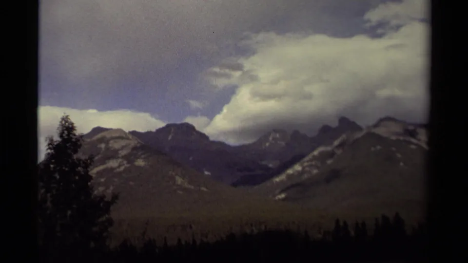 1979 8mm view of a Canadian forested valley with mountain peaks and a large pale cloud bank over the range.