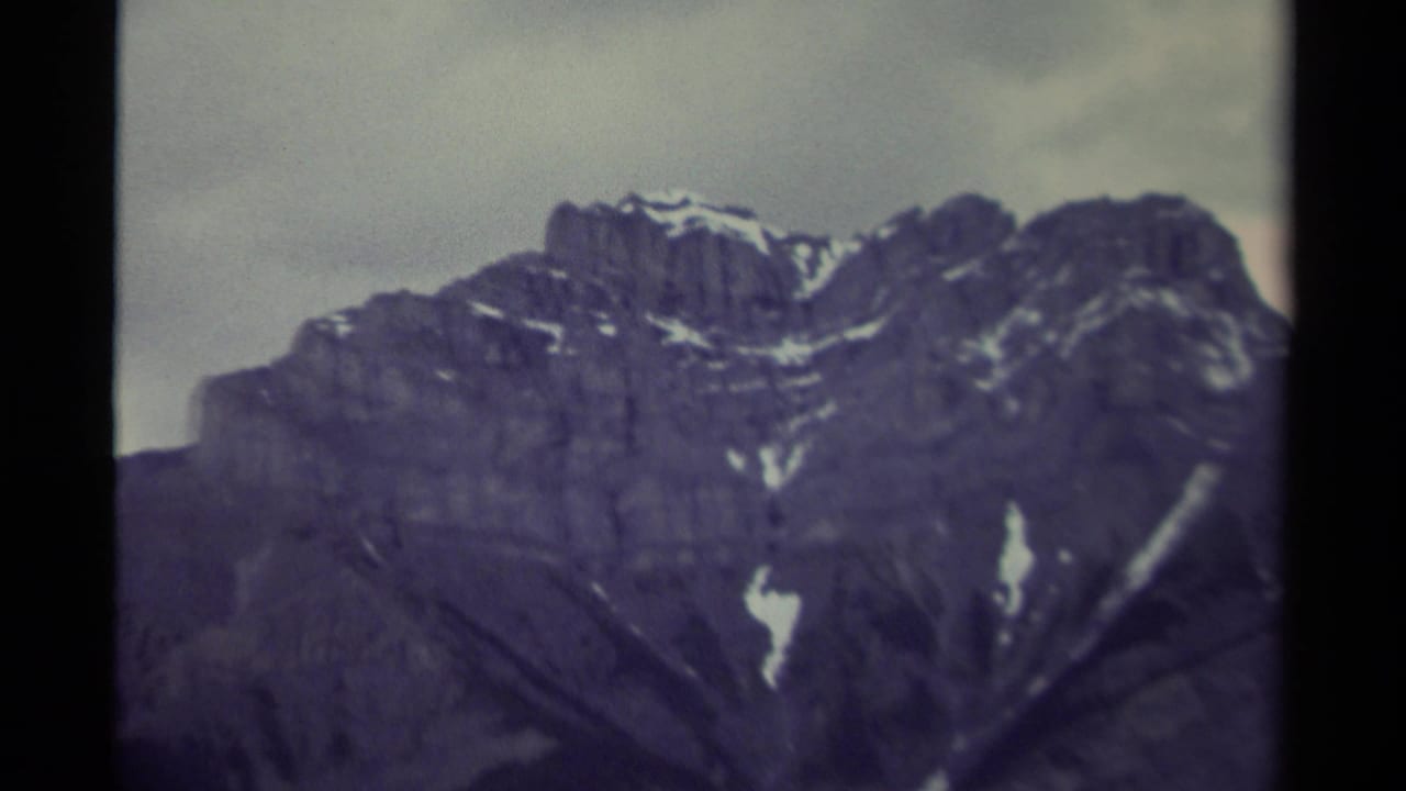 1979 8mm Canada footage showing a close view of a rugged mountain peak with snow streaks and dark cloud cover.