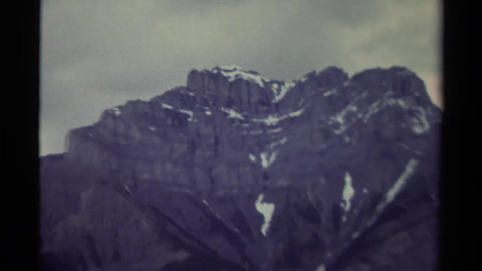 1979 8mm Canada footage showing a close view of a rugged mountain peak with snow streaks and dark cloud cover.