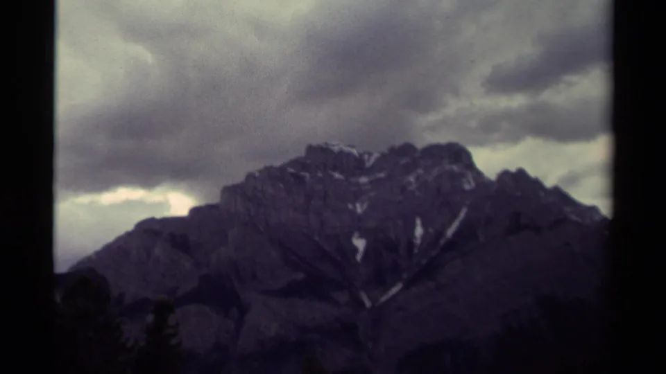 The final frame shows the Canadian mountain ridge in a wider 8mm view, with snow traces, heavy clouds, and dark foreground trees.