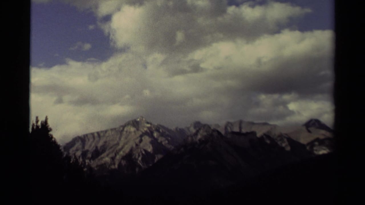 Mountain range under a bright cloud bank, with dark foreground trees and visible film-frame edges.