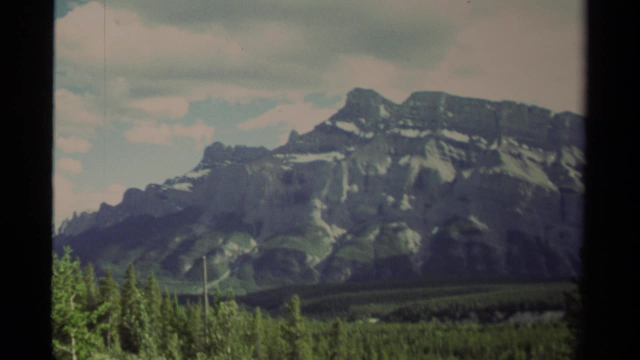 Broad gray mountain face with snow streaks above green conifer forest.