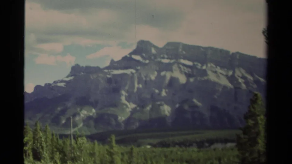 1979 Canada 8mm frame showing a snow-streaked mountain ridge beyond evergreen forest, with dark vertical film borders visible.