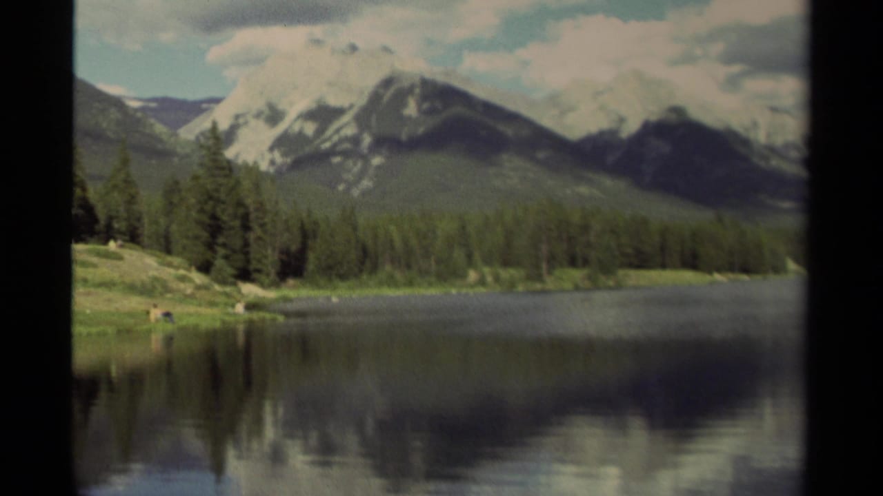 Snow-capped mountains and evergreen forest reflected in a calm lake.