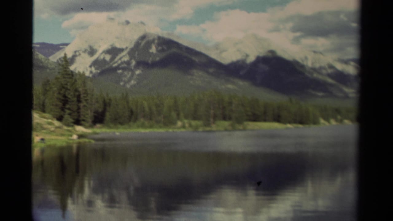 Evergreen shoreline and snowy mountain range reflected across a lake.