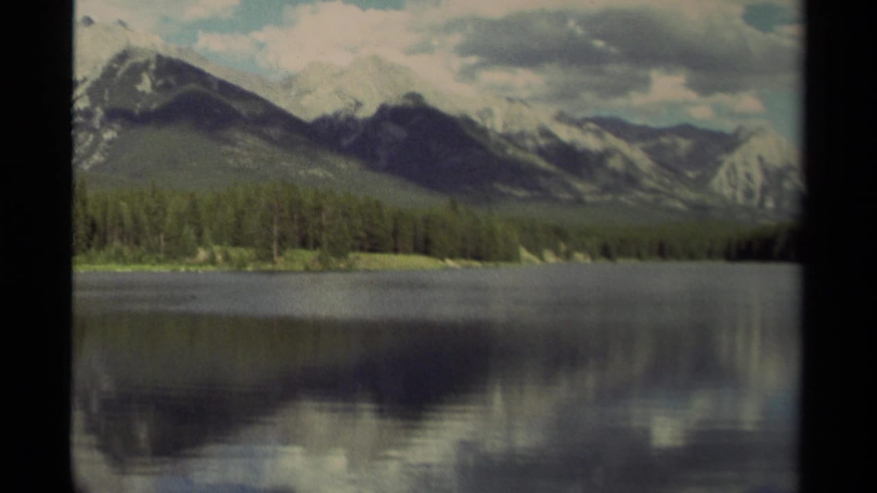 Calm lake reflecting clouds below forested mountains and dark 8mm frame edges.