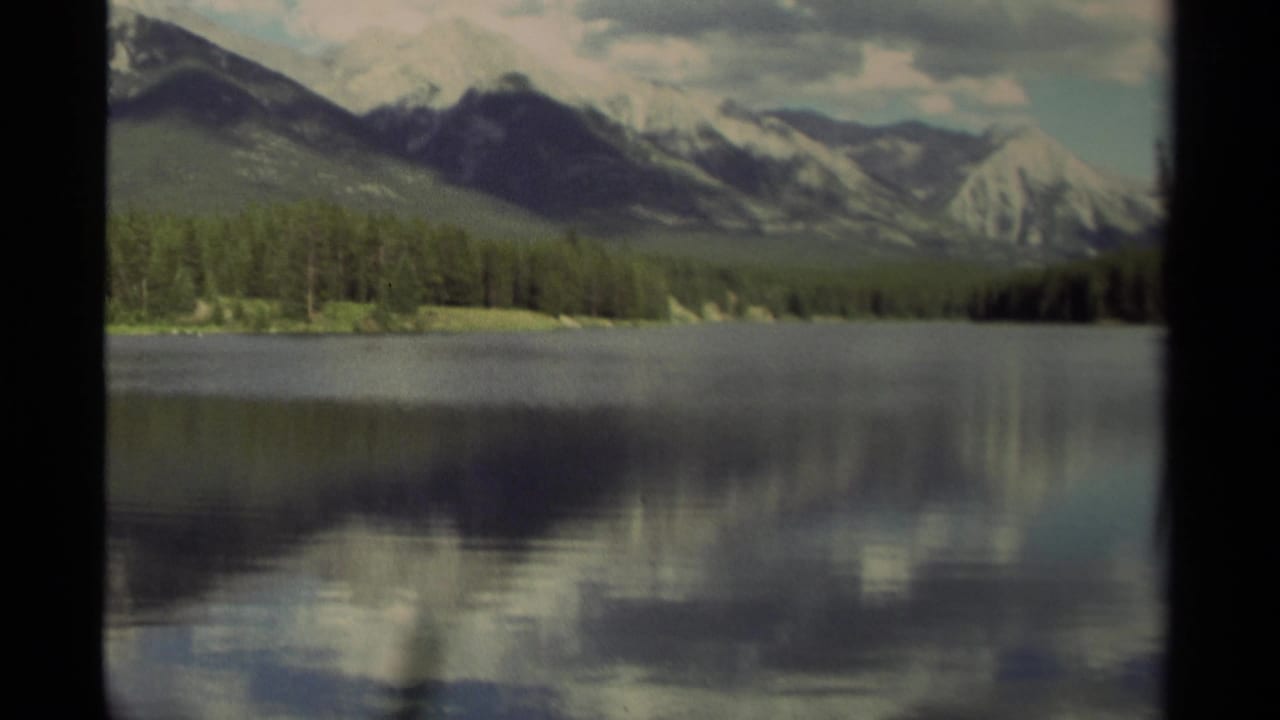 Mountain lake with forested shore, cloud reflections, and black film-frame borders.