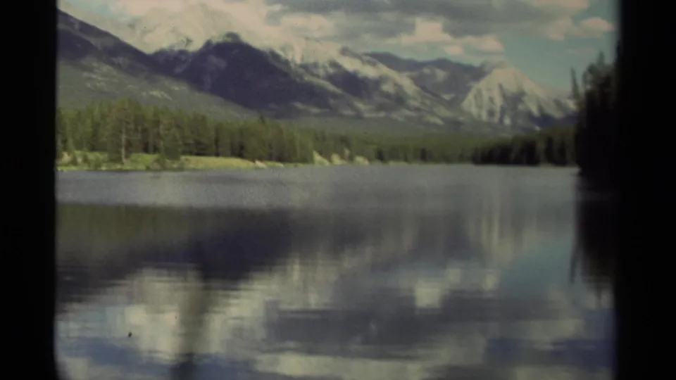 1979 Canada 8mm frame showing a soft-focus mountain lake scene with evergreen shoreline and muted sky reflections.
