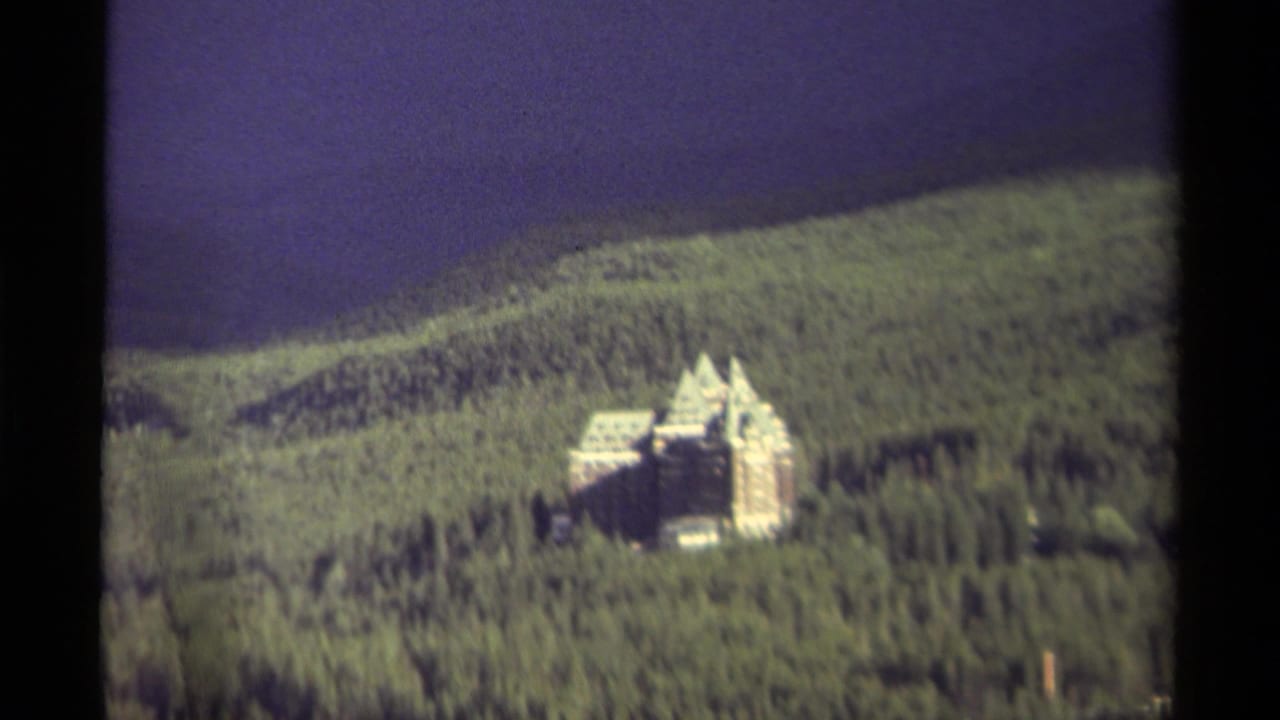 Distant pale castle-like mansion on a forested hillside beneath a dark sky.