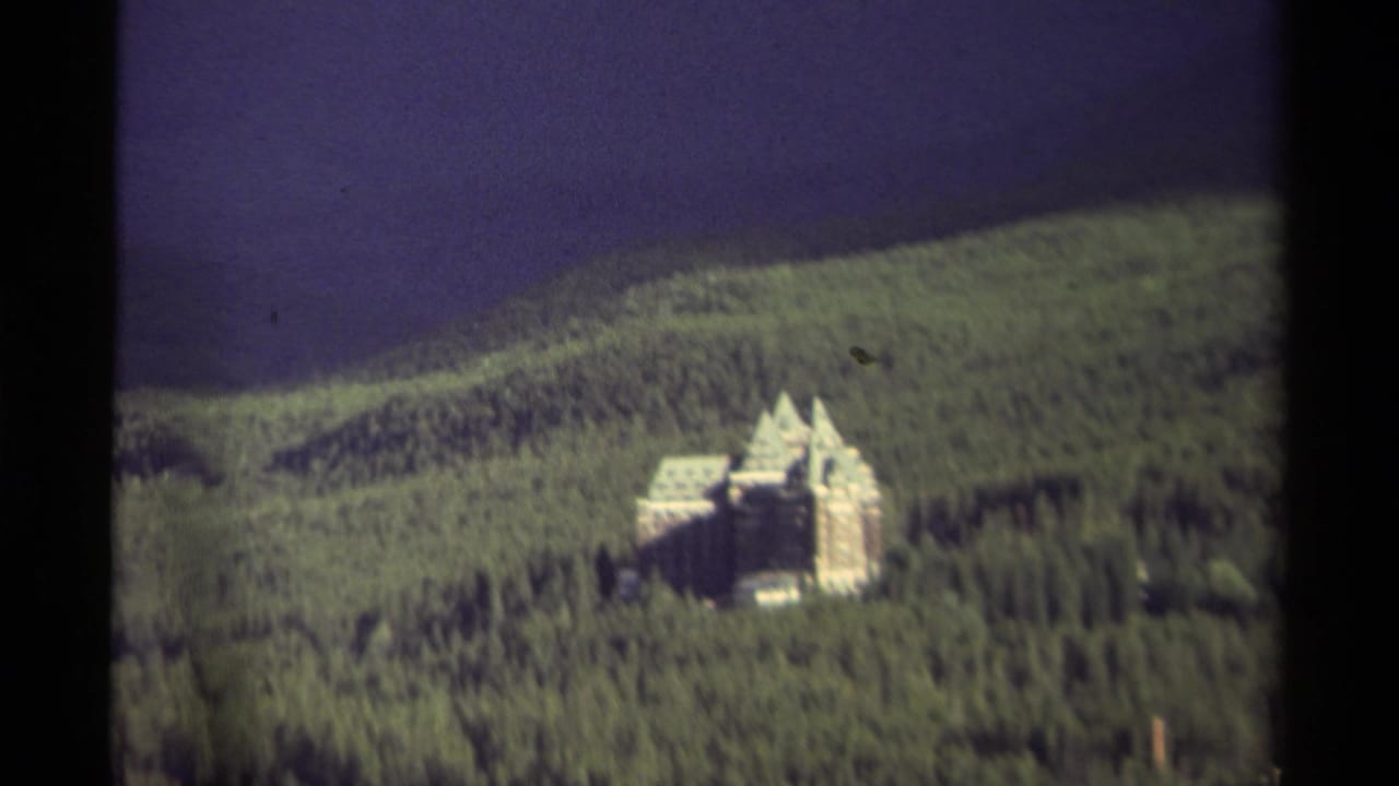 Castle-like mansion viewed from afar across dense green forest.