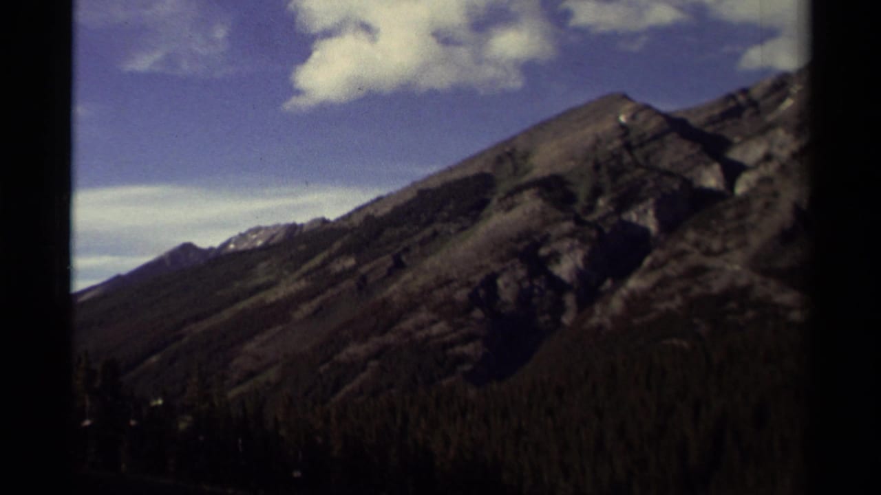 Rugged mountain slope above a dark forest under blue sky and white clouds.