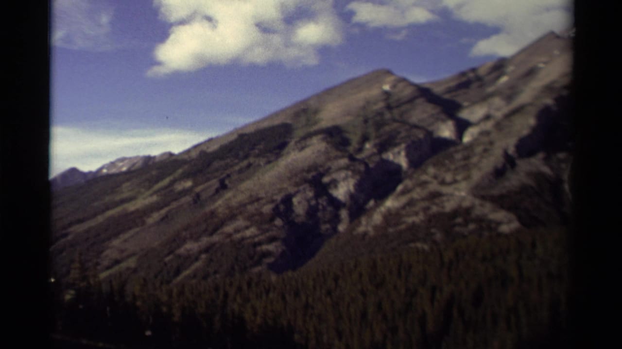 Rocky mountain ridge with forest below and clouds crossing a blue sky.
