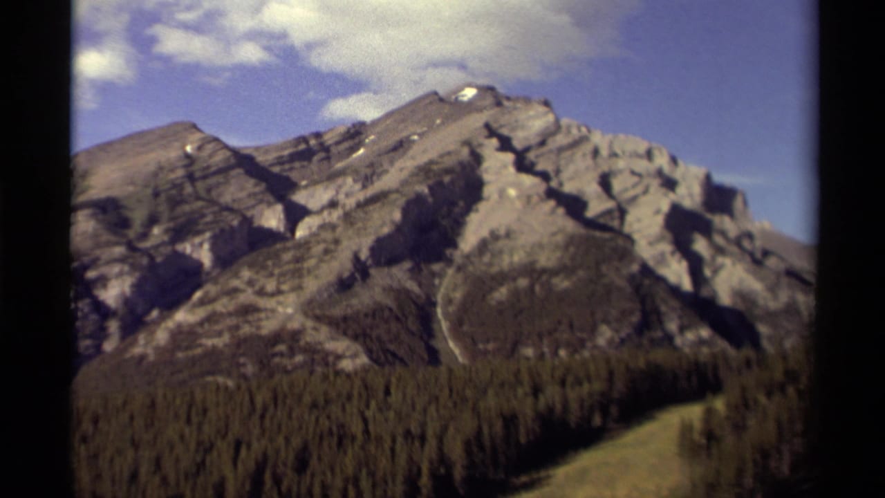 Mountain ridge and forest seen through dark film-frame borders under a bright sky.